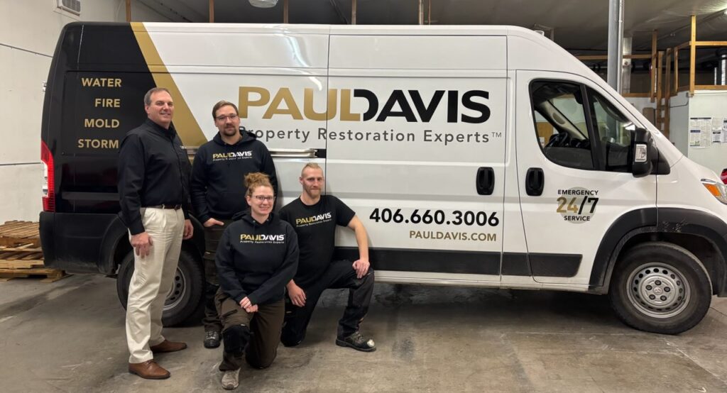 Paul Davis Restoration of Greater Missoula team posing inside a facility next to a branded service van displaying water, fire, mold, and storm damage restoration services with 24/7 emergency response.
