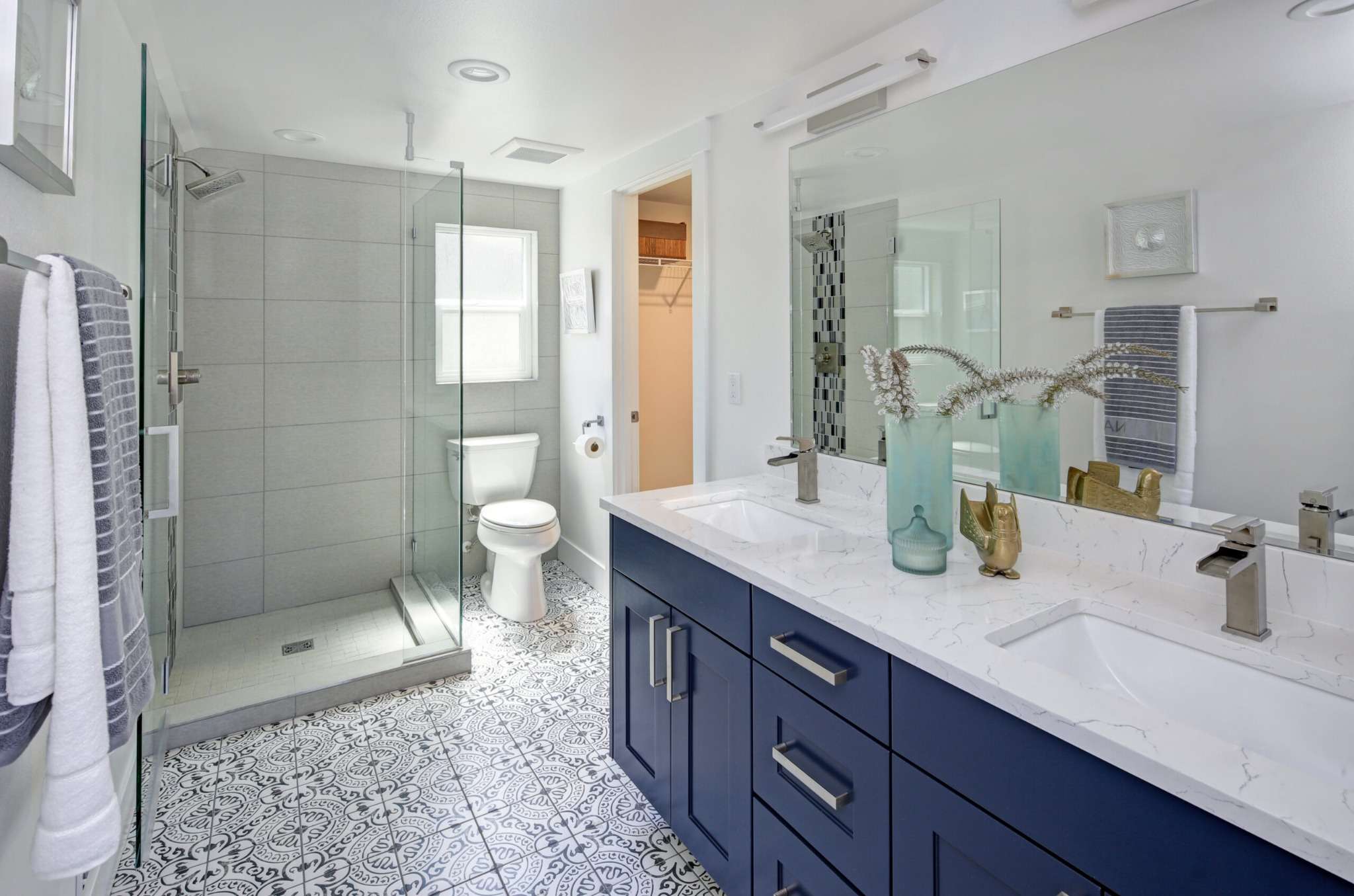 Modern bathroom remodel with blue double vanity, quartz countertop, patterned tile flooring, and glass walk-in shower in Greater Missoula.